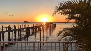 Een zonsondergang boven een rustig wateroppervlak, met een houten steiger die het water in reikt.