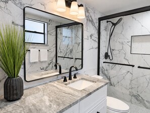 Een moderne badkamer met een marmeren spatwand, een grote spiegel, een wastafel met zwarte kraanwerk en een douchegedeelte.