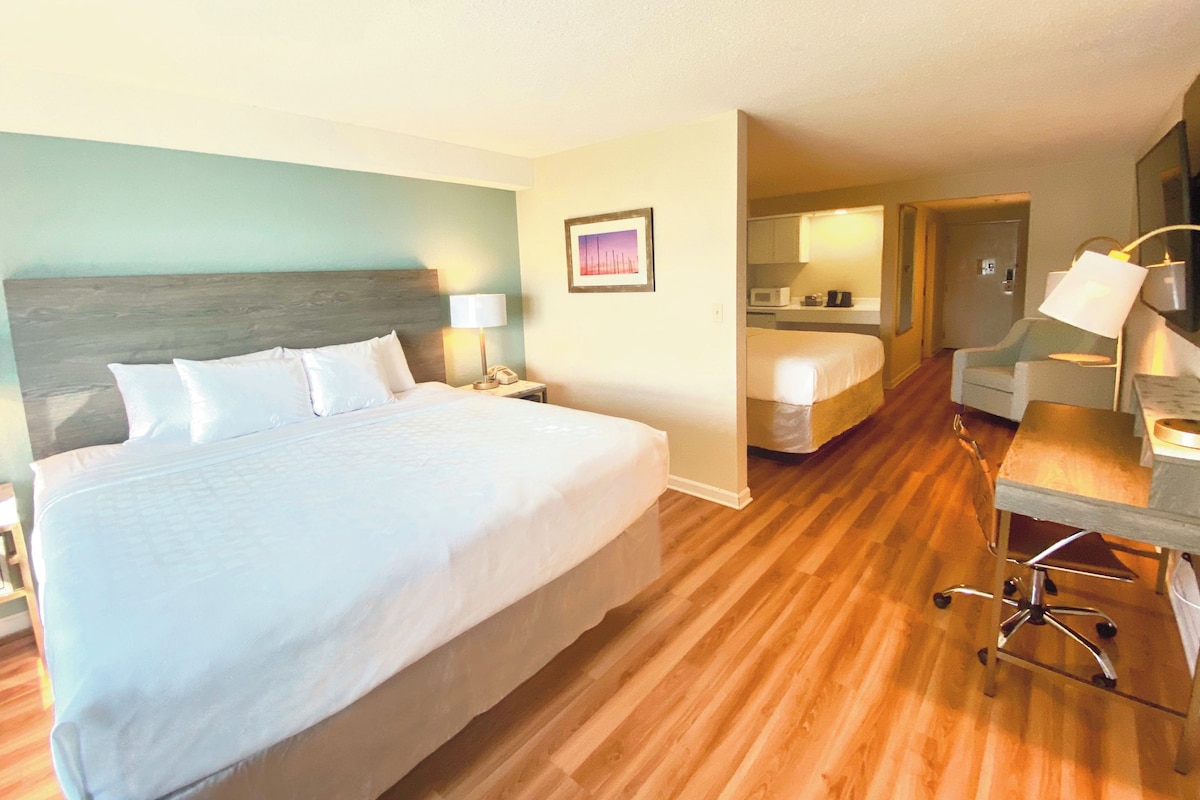 A hotel room with a large bed, a desk with a chair, a desk lamp, a telephone, and a picture on the wall.