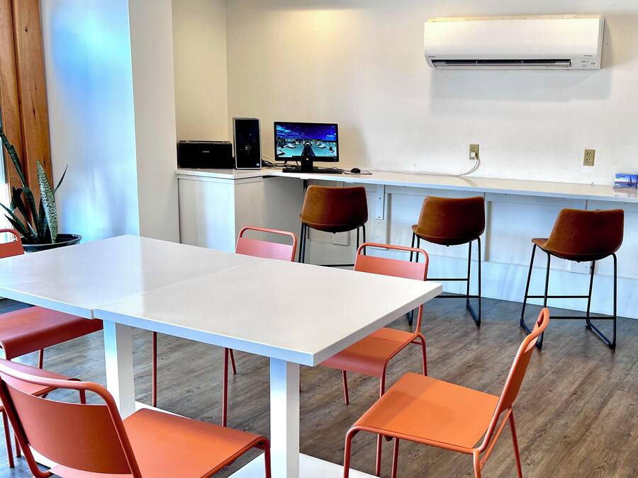A modern meeting room with a white table and orange chairs, a computer setup, and an air conditioning unit on the wall.