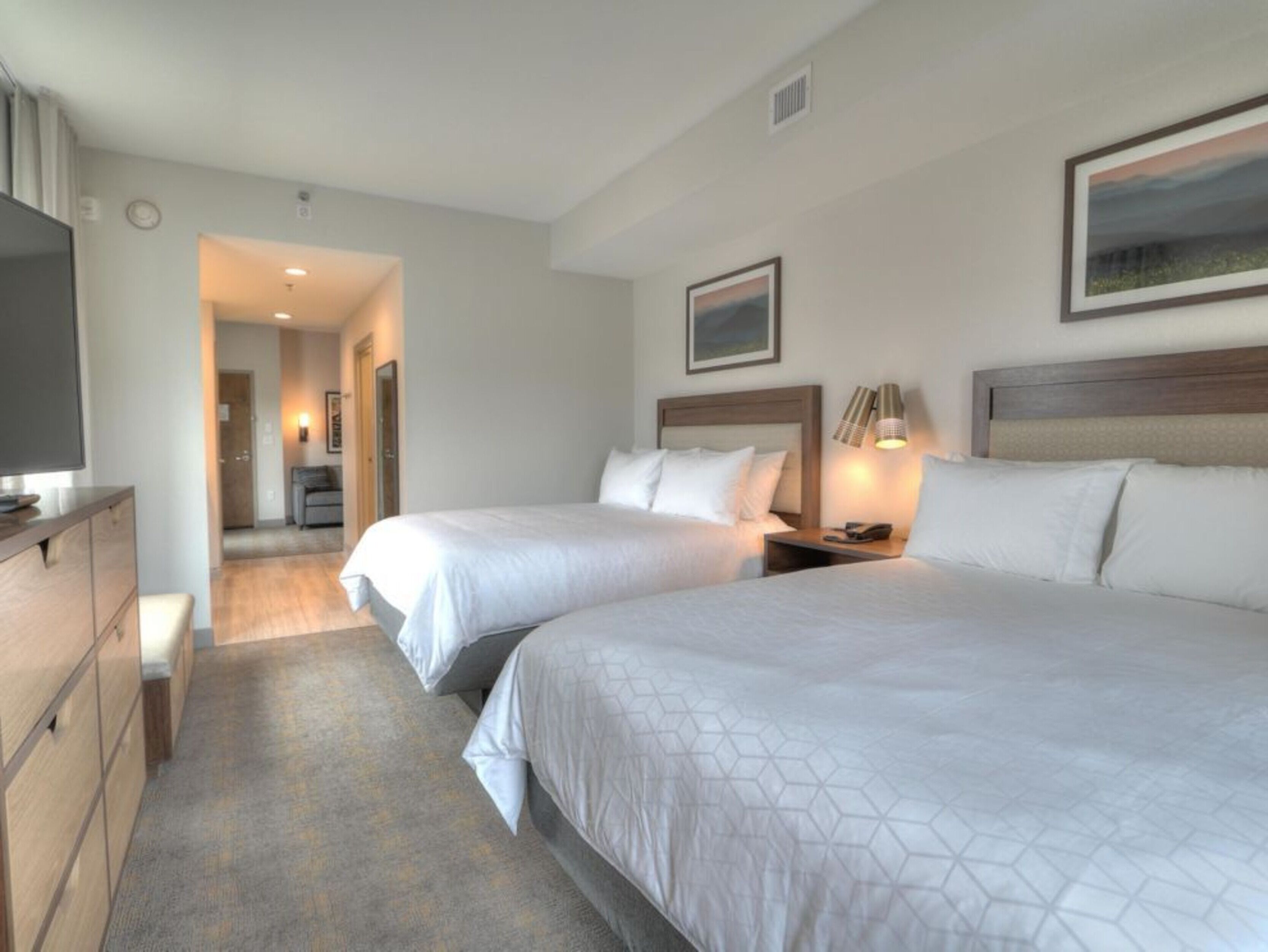 A hotel room with two beds, a TV, a desk, and a painting on the wall.