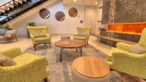 A lobby with a staircase, round wall decor, a fireplace, and green upholstered chairs. - Holiday Inn & Suites Pigeon Forge Convention Center by IHG (Pigeon Forge)