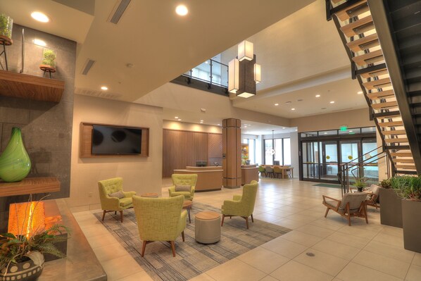 A spacious lobby with a reception desk, seating area with chairs, a staircase, and a large TV screen. - Holiday Inn & Suites Pigeon Forge Convention Center by IHG (Pigeon Forge)