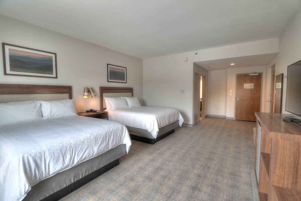 A hotel room with two beds, a desk, a TV, and a door leading to another room.