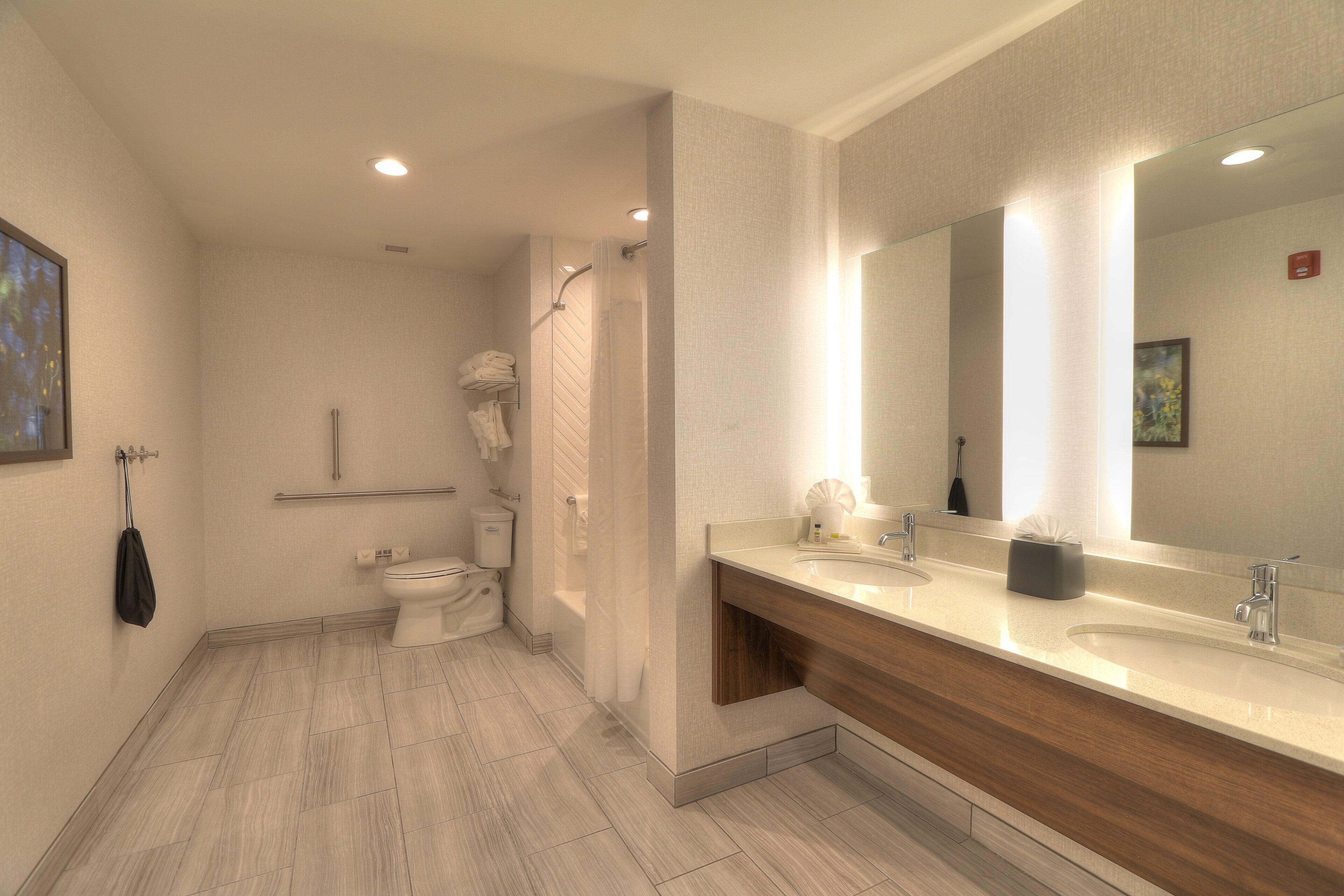 A modern bathroom with a large mirror, two sinks, and a shower area.
