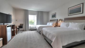 Ein Hotelzimmer mit zwei Betten, einem Schreibtisch, einem Fernseher und einem fenster mit Vorhängen.
