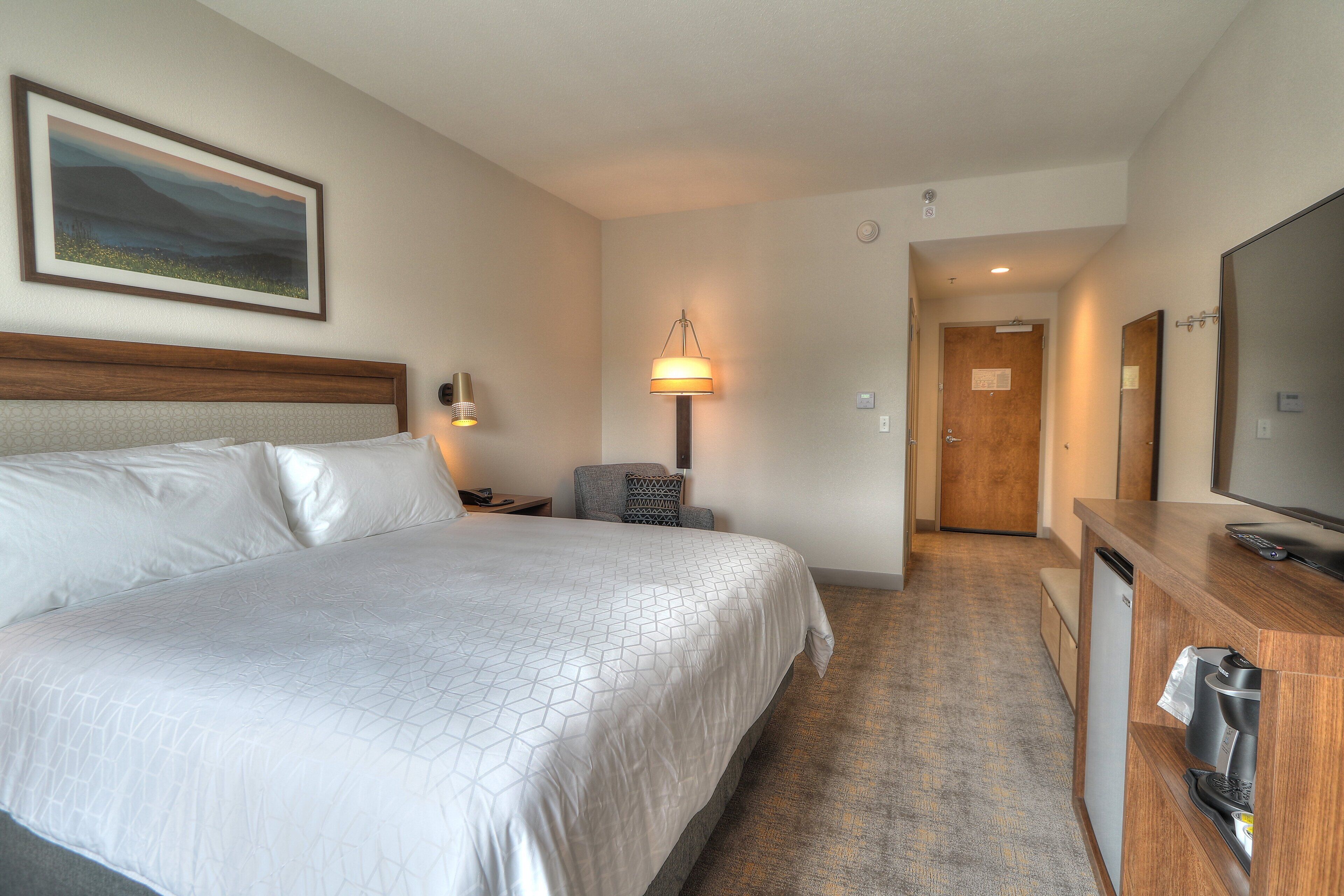A hotel room with a large bed, a desk with a coffee maker, a television, and a painting on the wall.