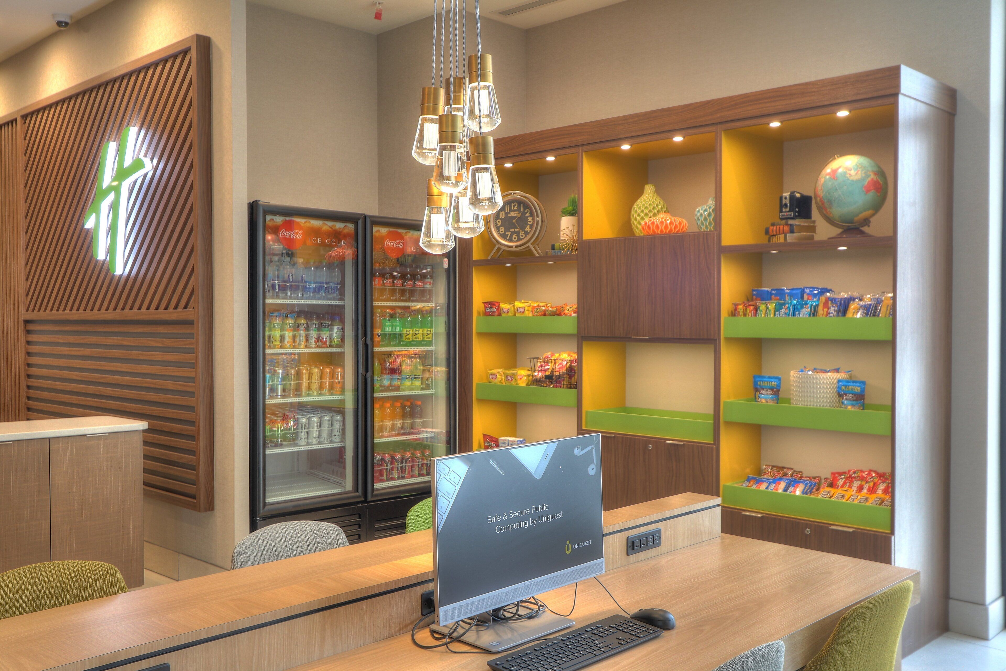 Un área de recepción moderna con un escritorio de ordenador, asientos, un refrigerador de Coca-Cola y estantes con aperitivos y un globo terráqueo.