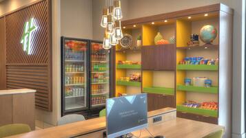 Un área de recepción moderna con un escritorio de ordenador, asientos, un refrigerador de Coca-Cola y estantes con aperitivos y un globo terráqueo.