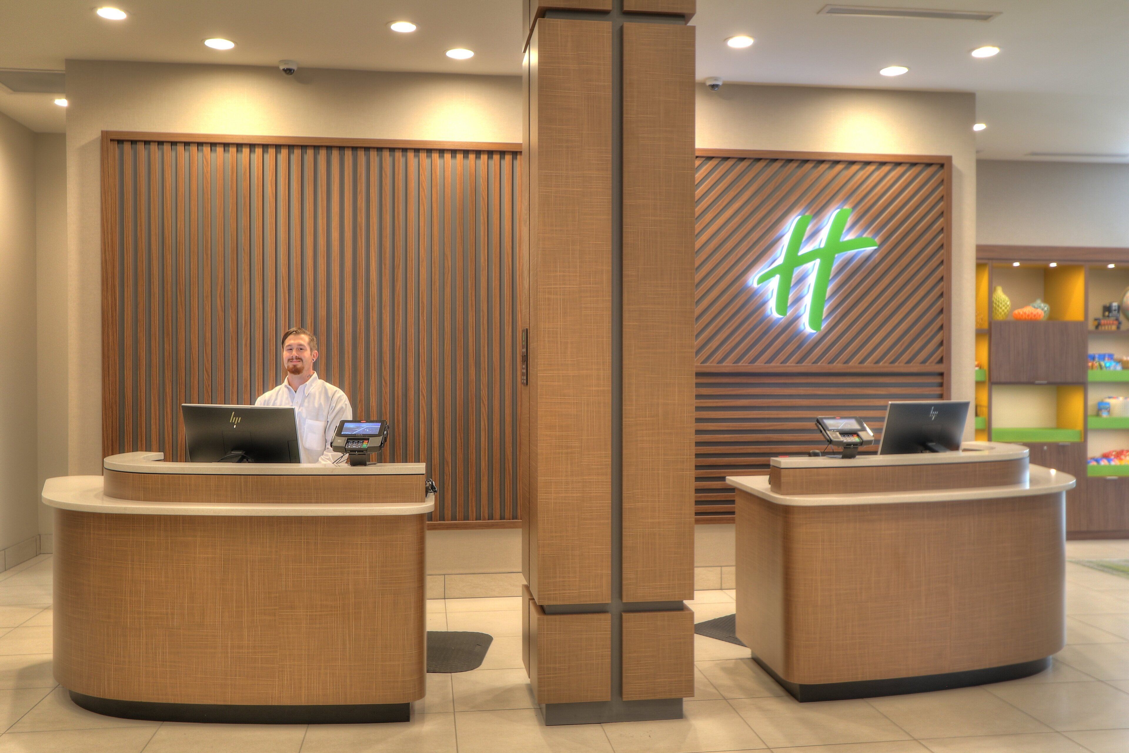 A reception area with two desks, each with a laptop and a phone. There is a large wooden panel with a logo in the background.