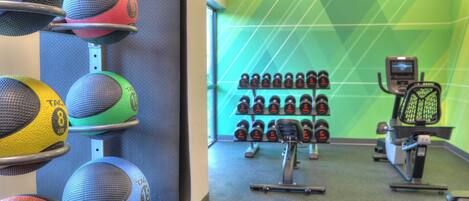 A gym with exercise equipment, including a wall-mounted rack of dumbbells and a row of medicine balls.