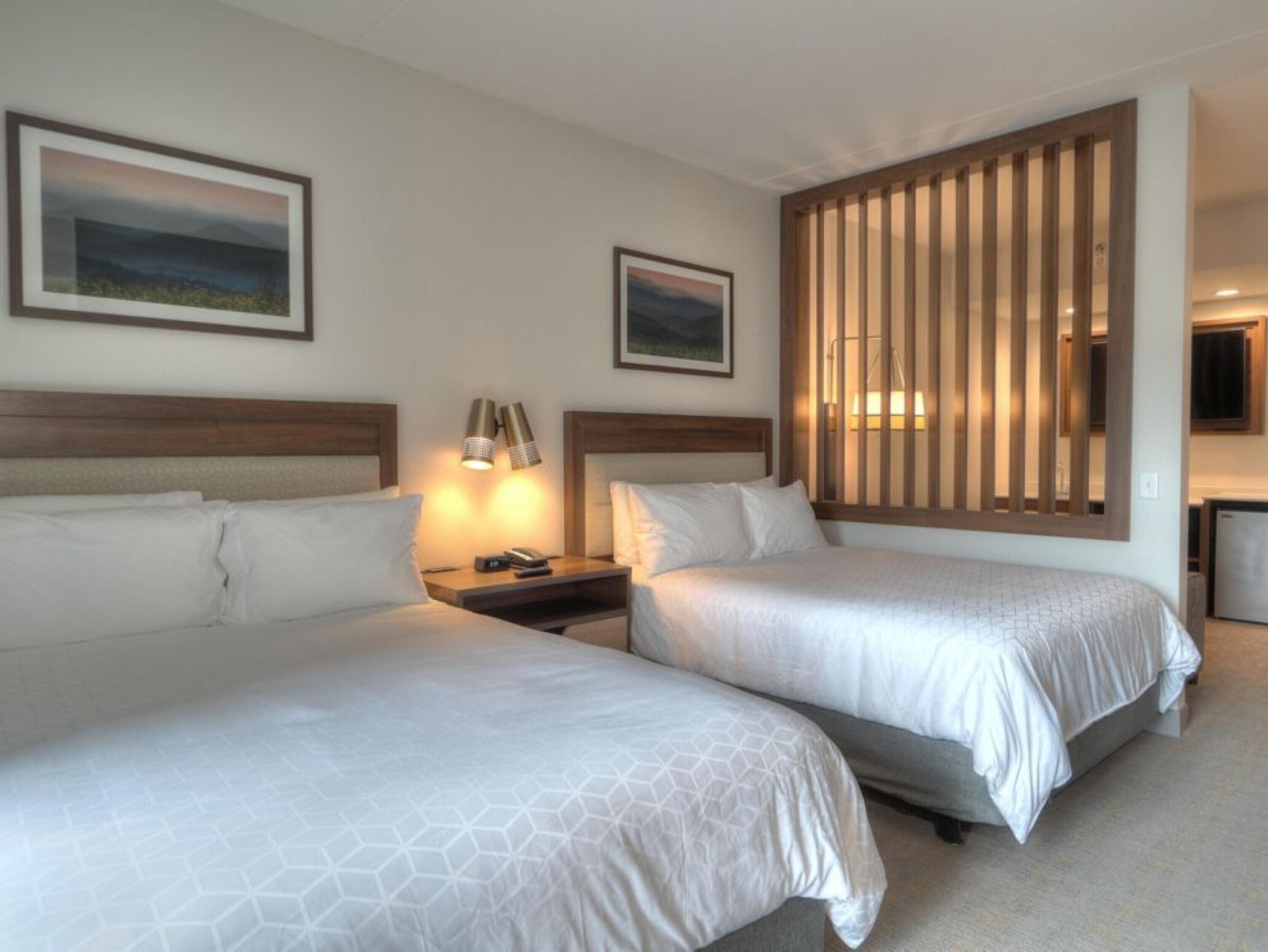 A hotel room with two beds, a nightstand with a lamp, and a wooden partition.