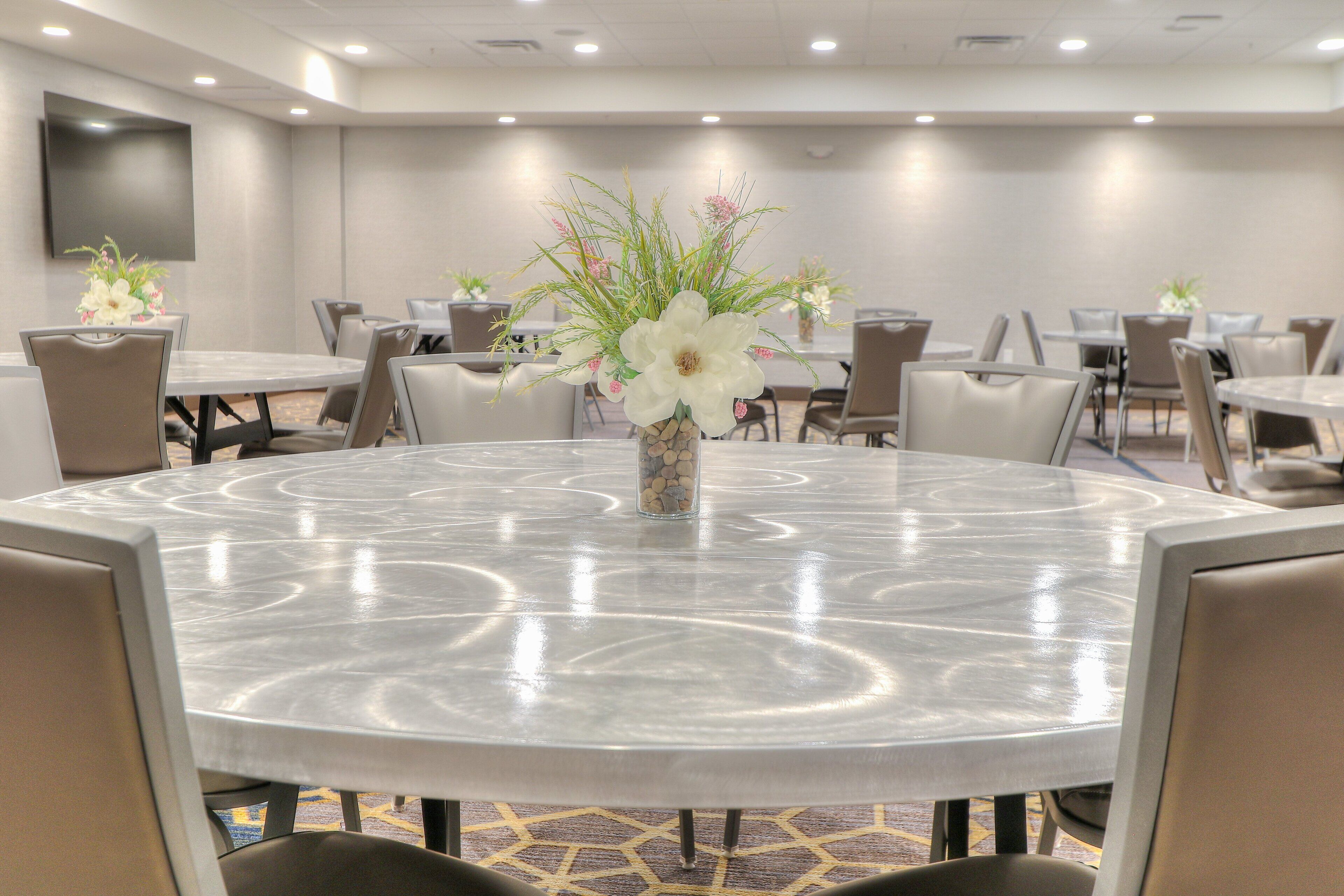 A conference room with round tables, chairs, and a large vase with flowers.