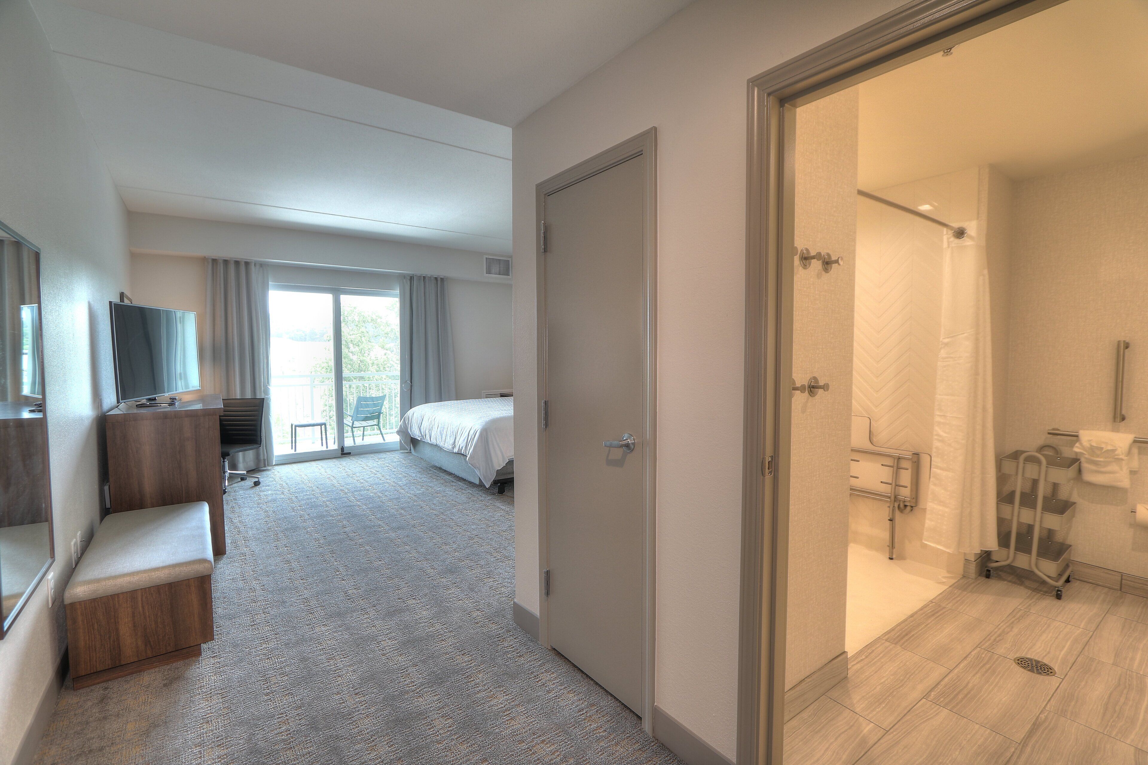 A hotel room with a bed, a desk, a TV, a shower, and a bathroom.