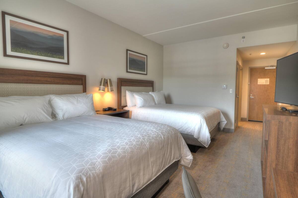 A hotel room with two beds, a TV, and a door leading to a bathroom.
