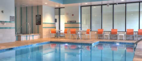 Una piscina interior con agua azul cristalina, rodeada de sillas anaranjadas y blancas, y un cartel que dice 'NO DIVING' en la pared.
