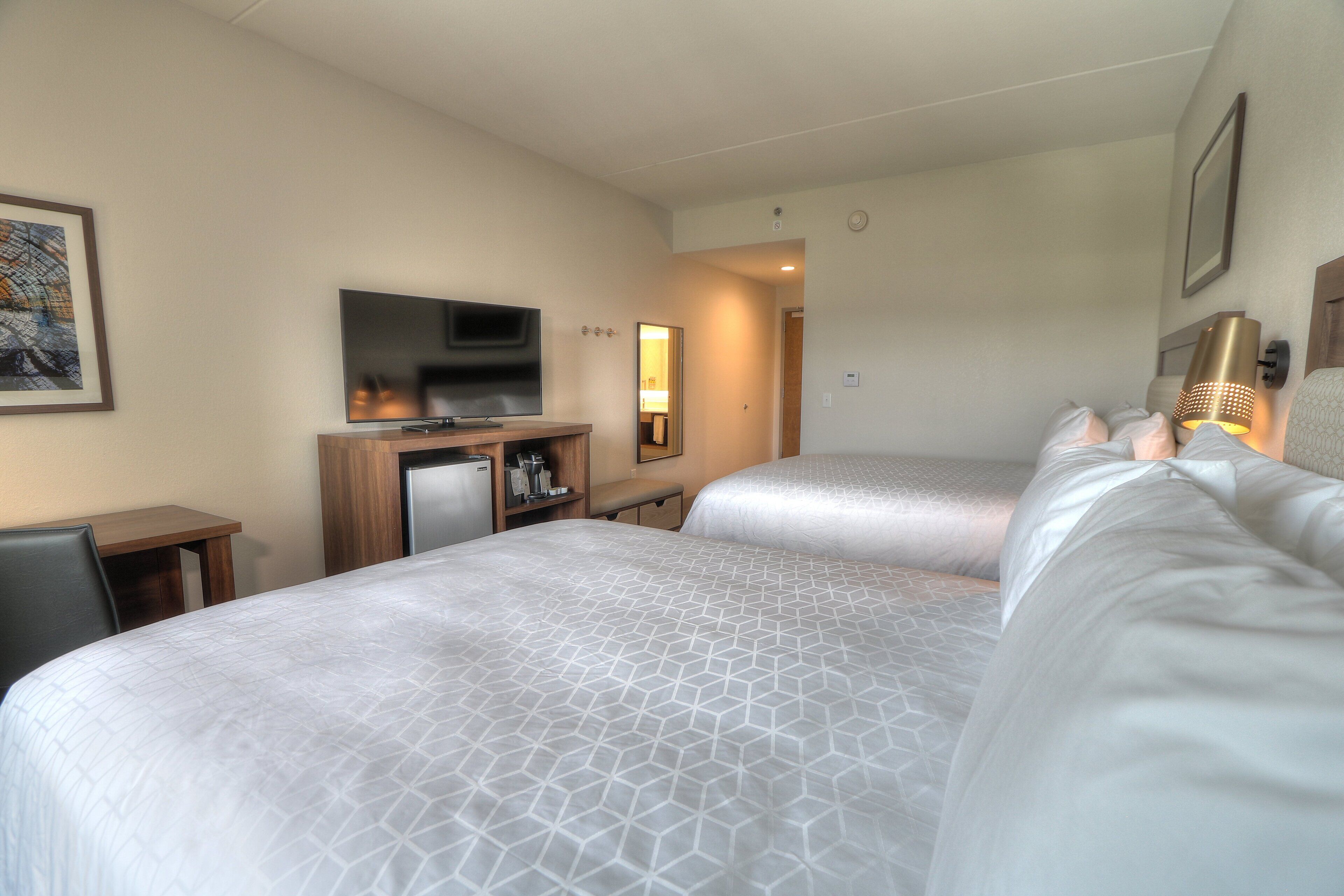 A hotel room with two beds, a TV, a desk, and a small kitchenette.