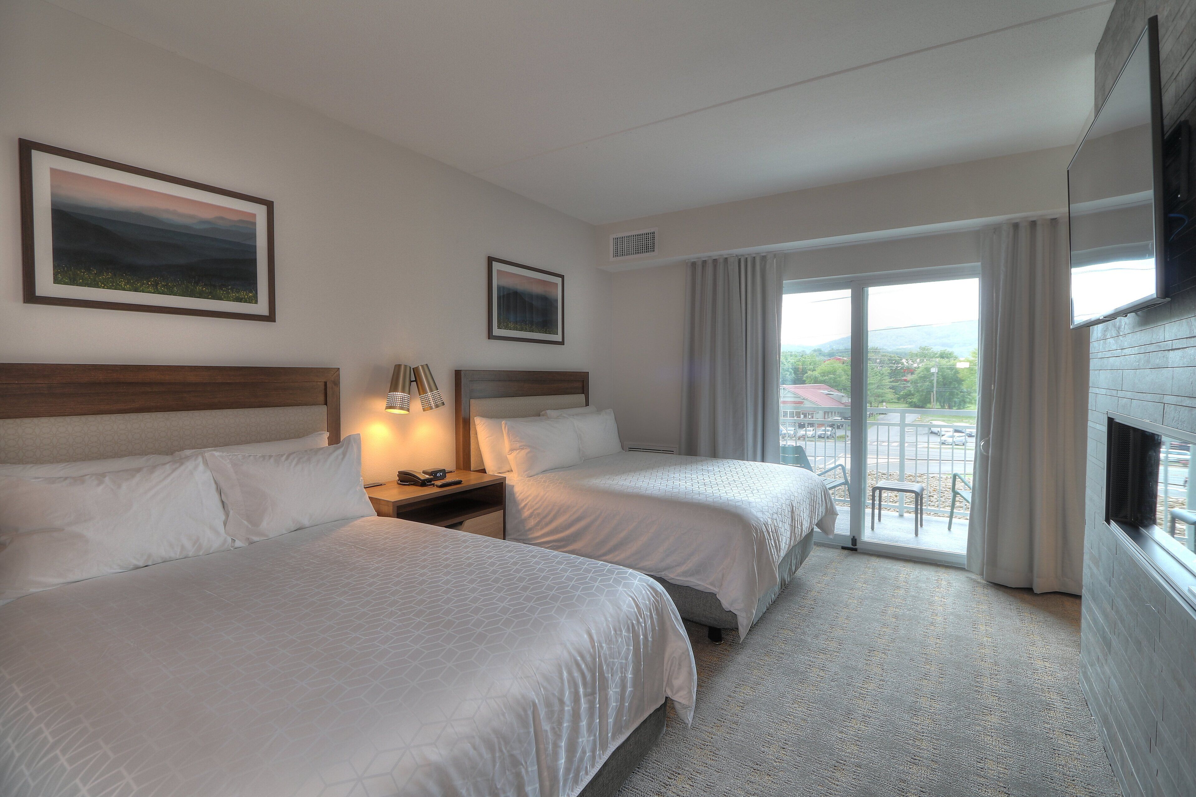 A hotel room with two beds, a TV, a window with curtains, and a view of the outside.