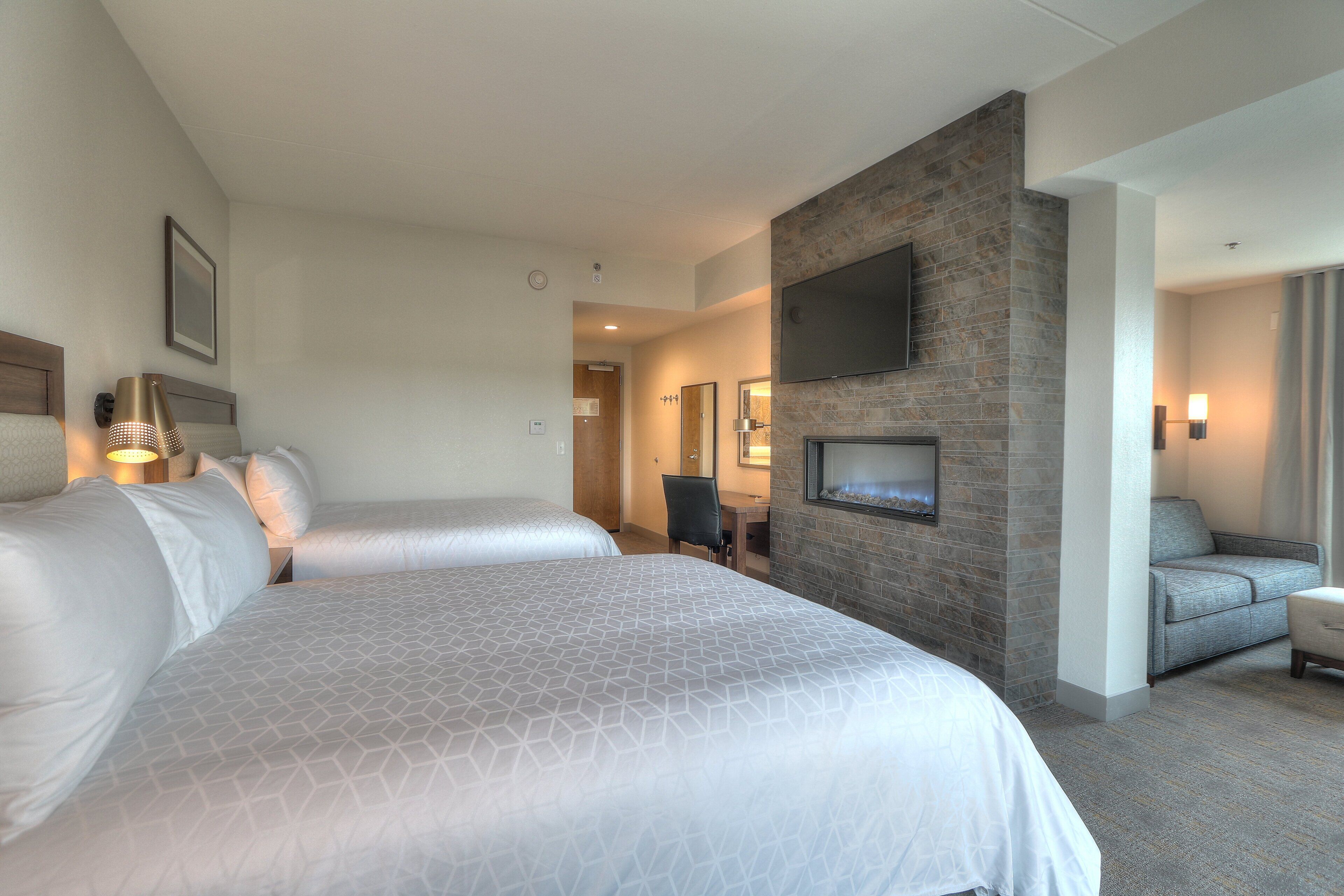 Habitación de hotel con dos camas, un televisor montado en una pared de piedra, un escritorio y una silla.