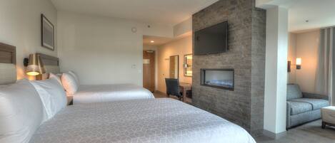 Habitación de hotel con dos camas, un televisor montado en una pared de piedra, un escritorio y una silla.
