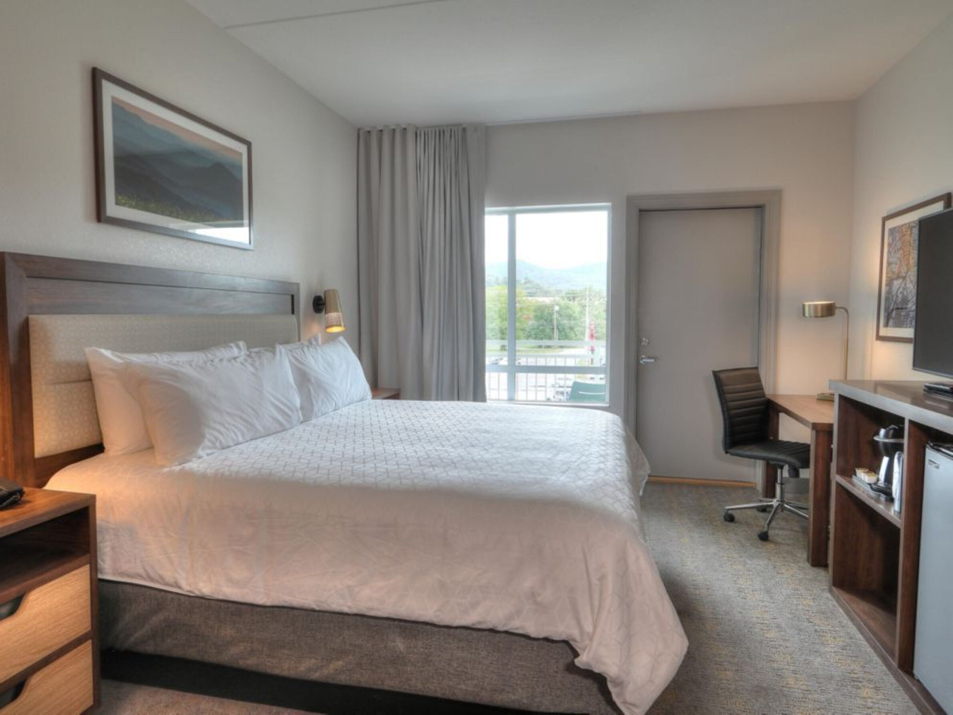 Habitación de hotel con una cama grande, un escritorio, una silla y un televisor.