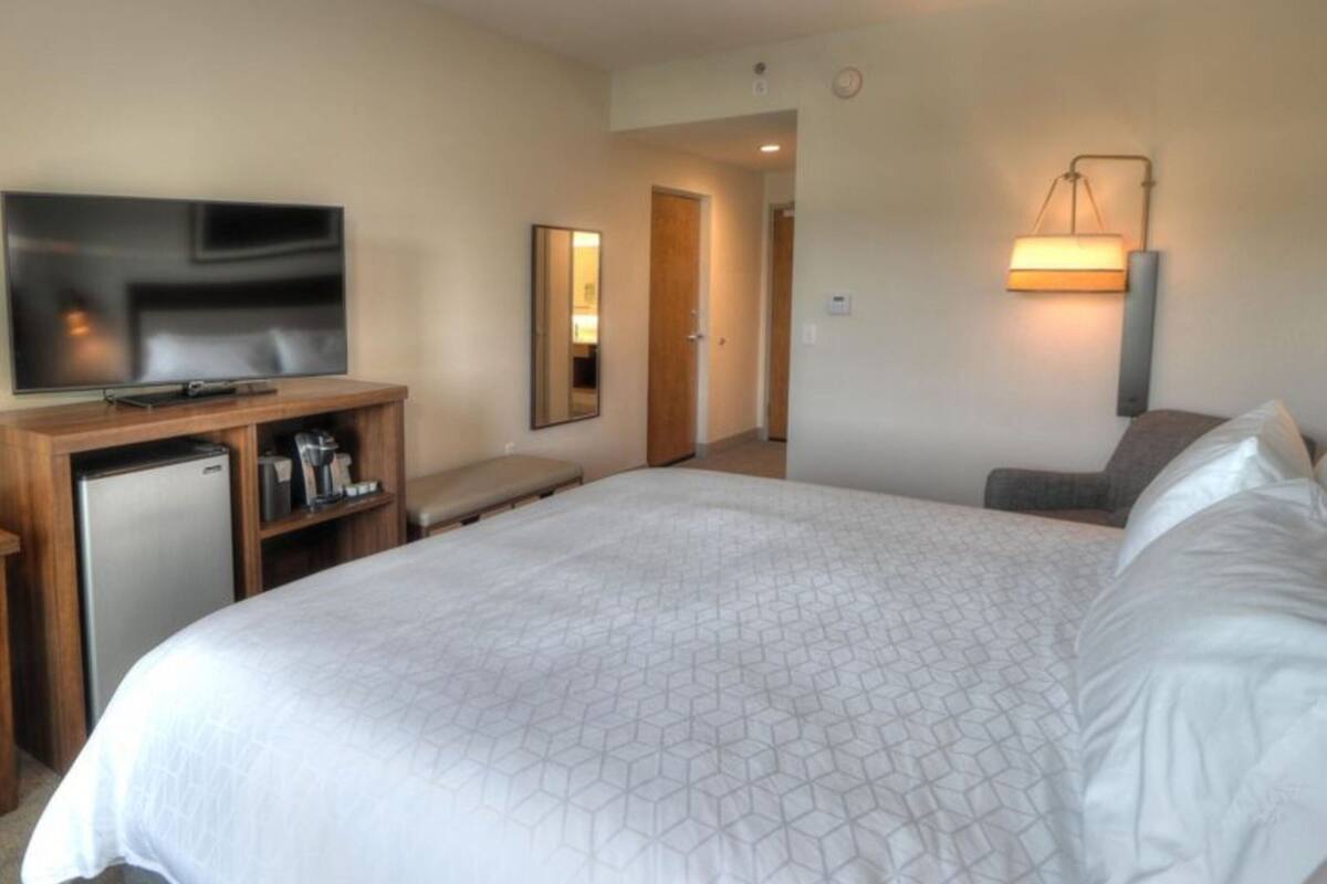 A hotel room with a large bed, a television, a desk with a computer, a refrigerator, and a mirror.