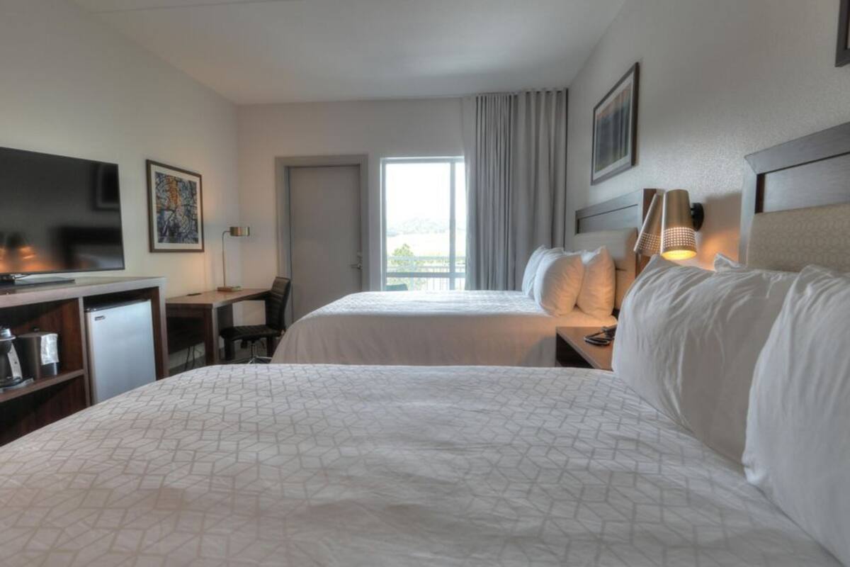 A hotel room with a large bed, a desk with a chair, a television, and a window with curtains.