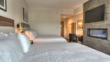 A hotel room with two beds, a fireplace, a television, and a desk.
