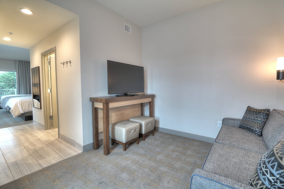 A modern hotel room with a wooden desk, a flat-screen TV, a sofa, and a large mirror.