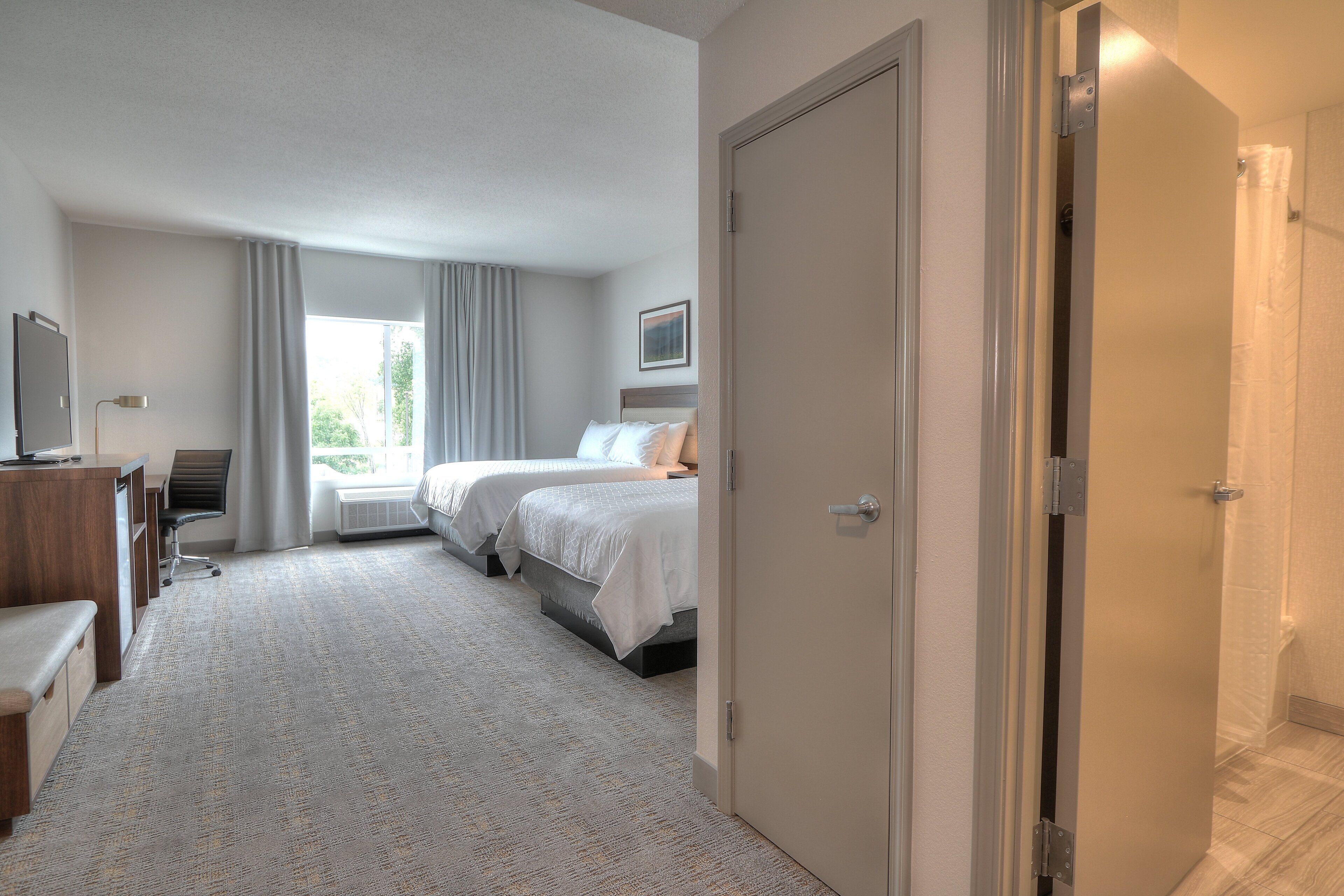A hotel room with two beds, a desk, and a chair.