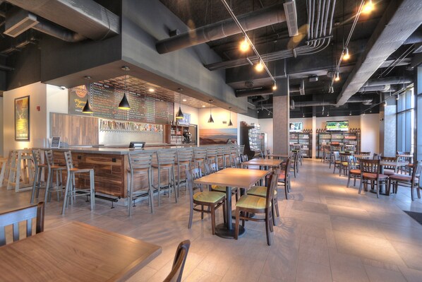 A modern cafe with a bar area, wooden tables and chairs, and a large window providing natural light. - Holiday Inn & Suites Pigeon Forge Convention Center by IHG (Pigeon Forge)
