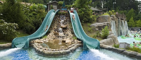 Parque acuático con dos toboganes, una cascada rocosa y una zona de piscina.