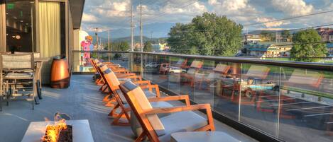 A rooftop lounge with a row of wooden lounge chairs and a fire feature.