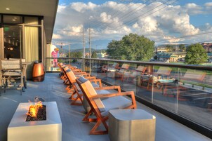 A rooftop lounge with a row of wooden lounge chairs and a fire feature.