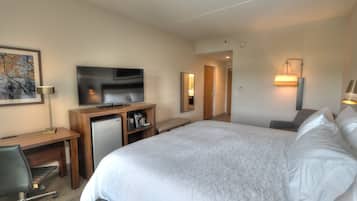 A hotel room with a bed, a desk with a television, a coffee machine, and a chair.