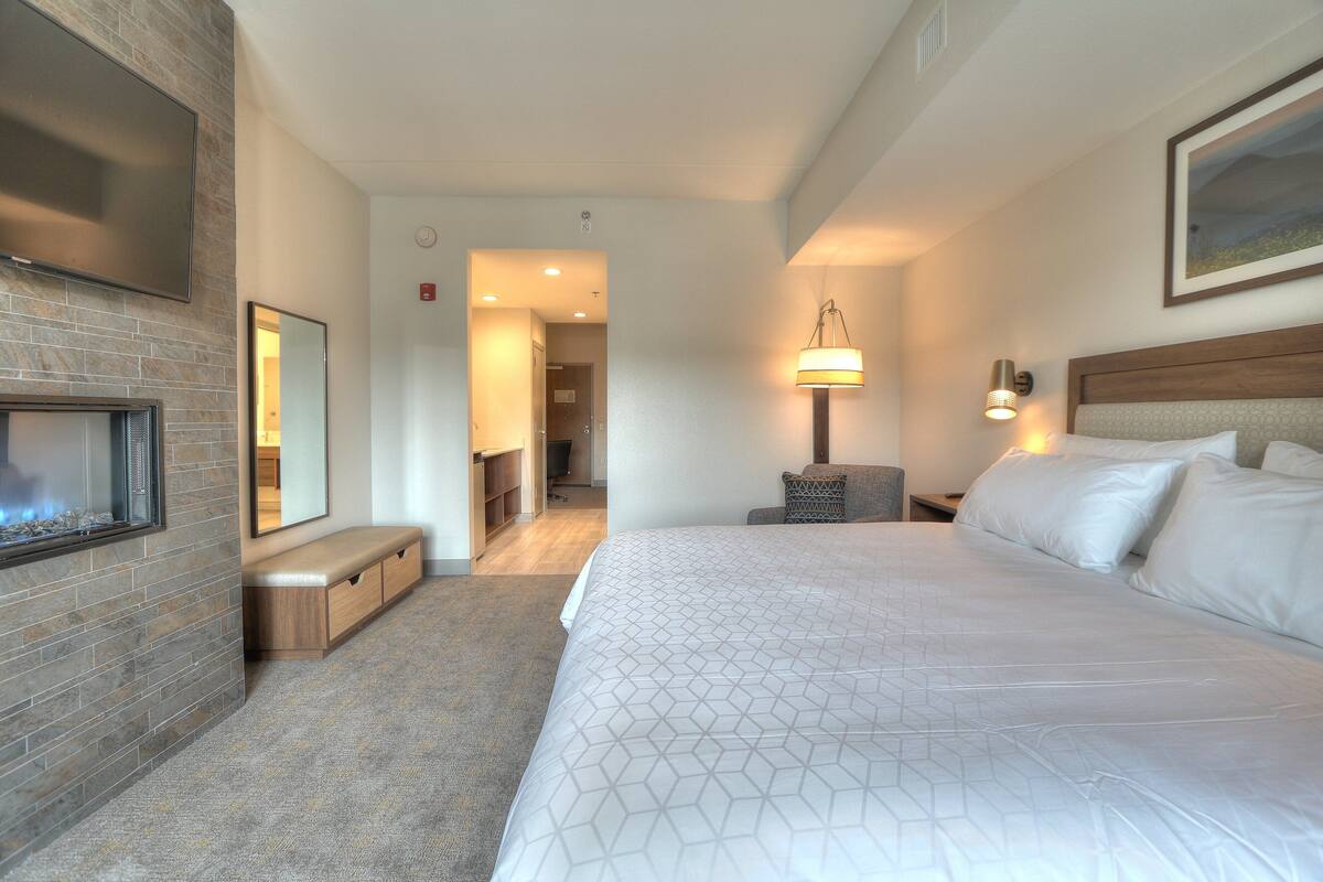 A hotel room with a large bed, a fireplace, a desk, and a lamp.