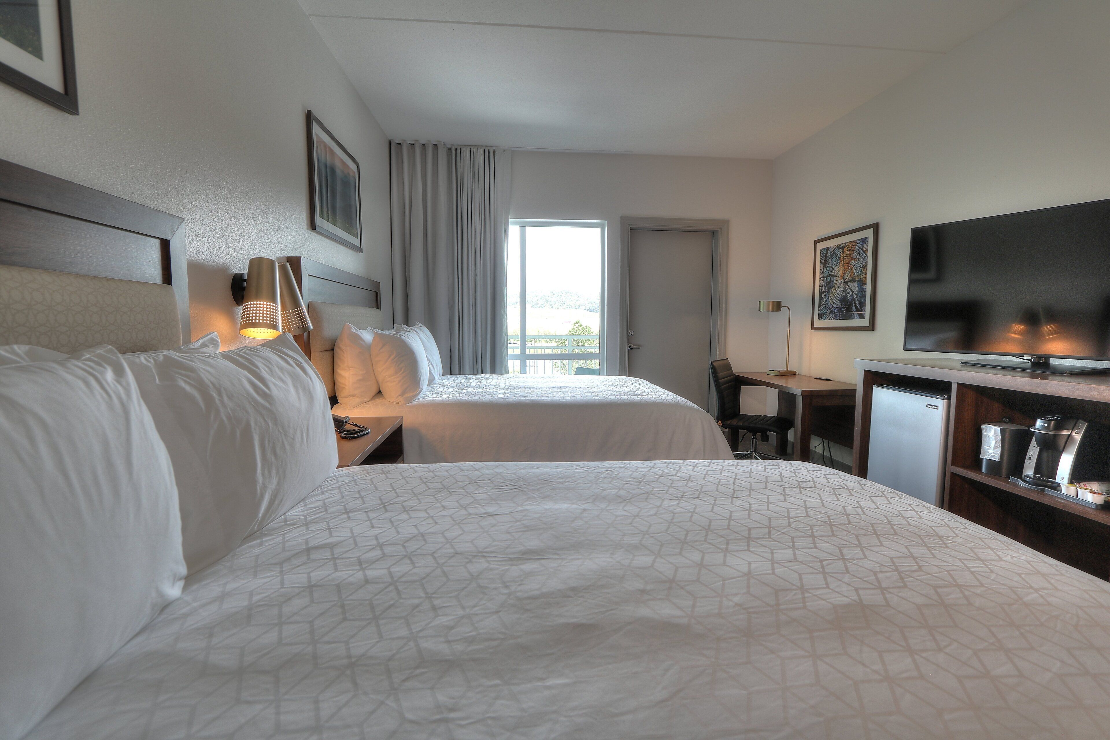 A hotel room with two beds, a desk, a TV, and a coffee machine.