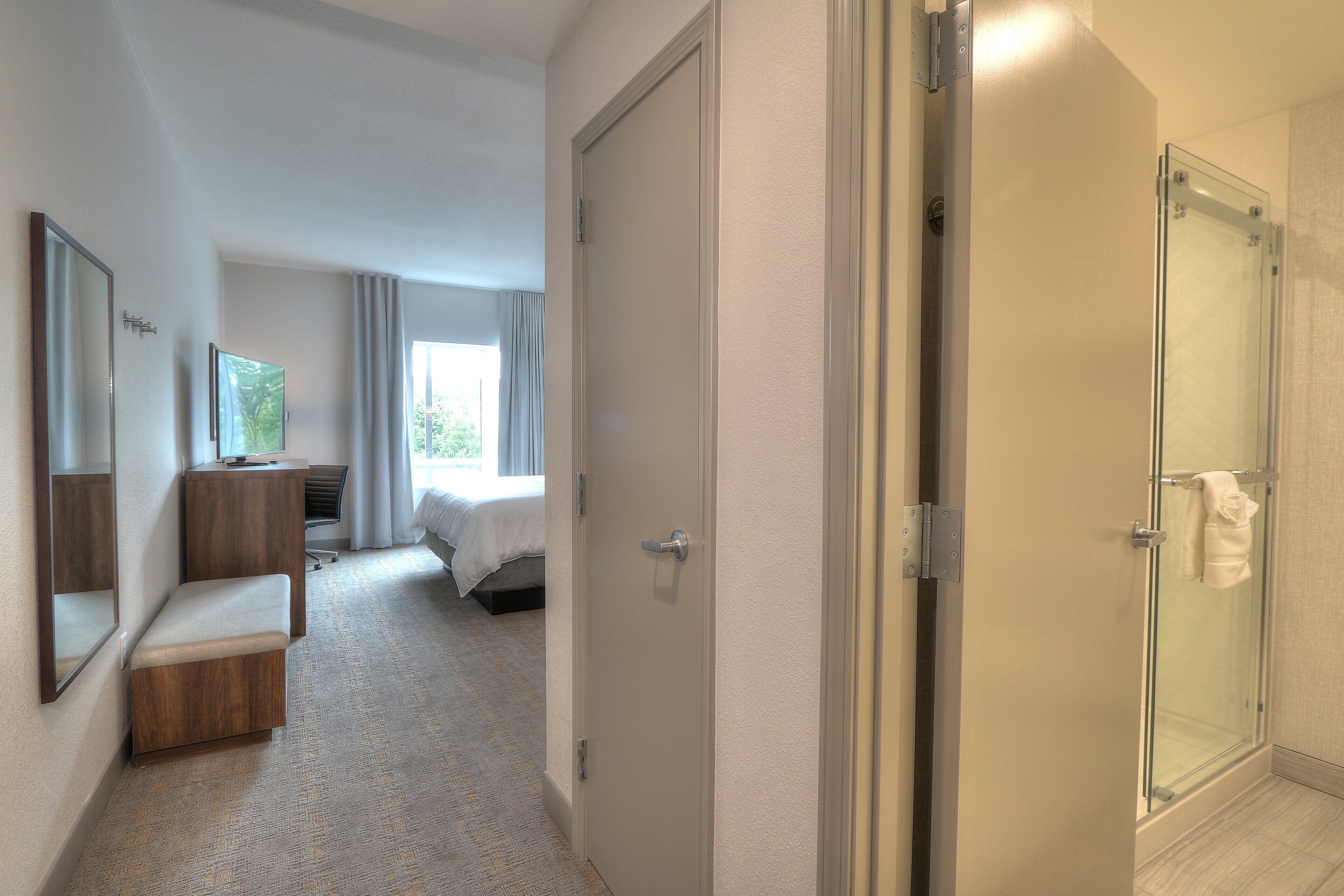 A hotel room with a shower, a bench, a desk, and a bed.