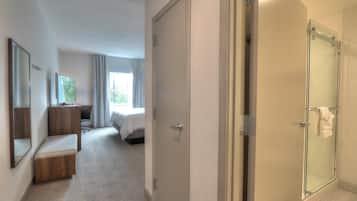 A hotel room with a shower, a bench, a desk, and a bed.