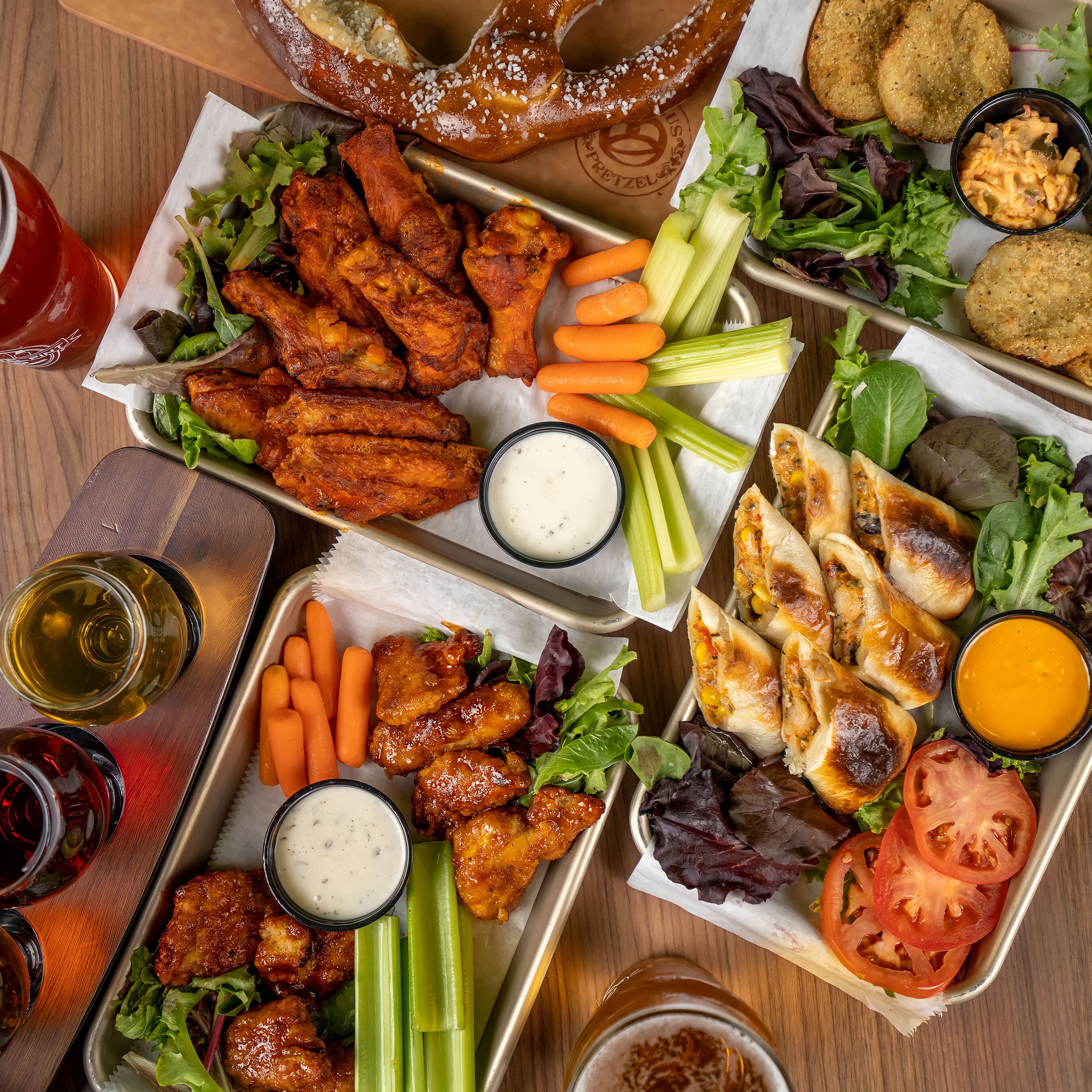 A variety of food items including wings, pretzels, and sandwiches, arranged on trays.