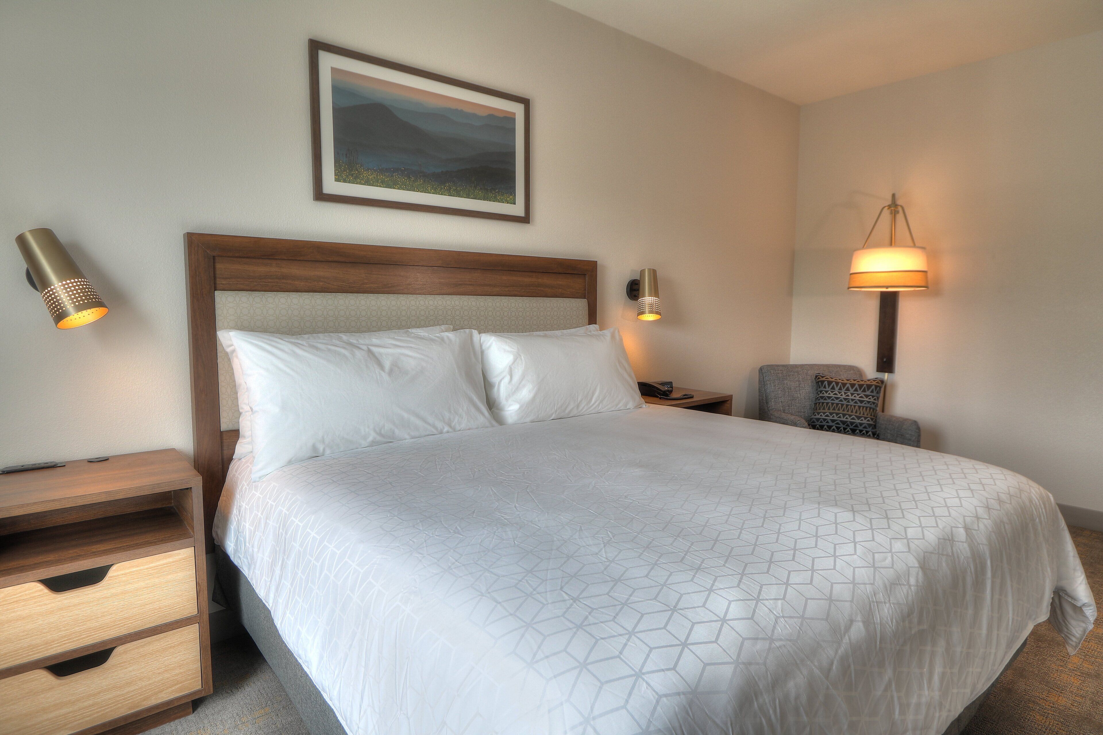 A neatly made bed with a geometric patterned bedspread, a wooden headboard, and two bedside tables with lamps.