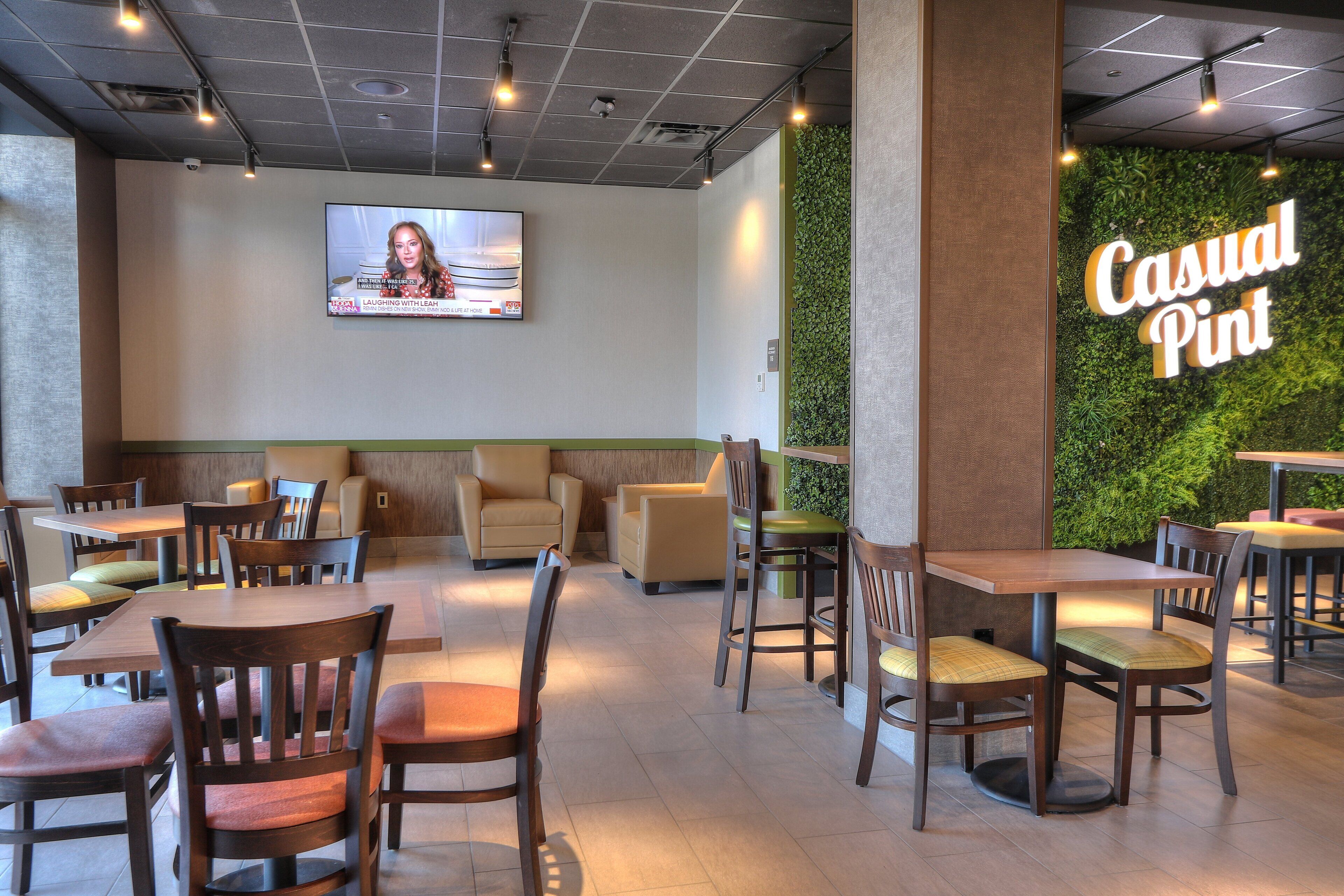 L’intérieur d’un restaurant présente plusieurs tables et chaises, un téléviseur fixé au mur et un mur vert sur lequel on peut lire le texte « Casual Pint ».