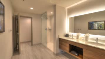 A modern bathroom with a large mirror, two sinks, and a shower area.