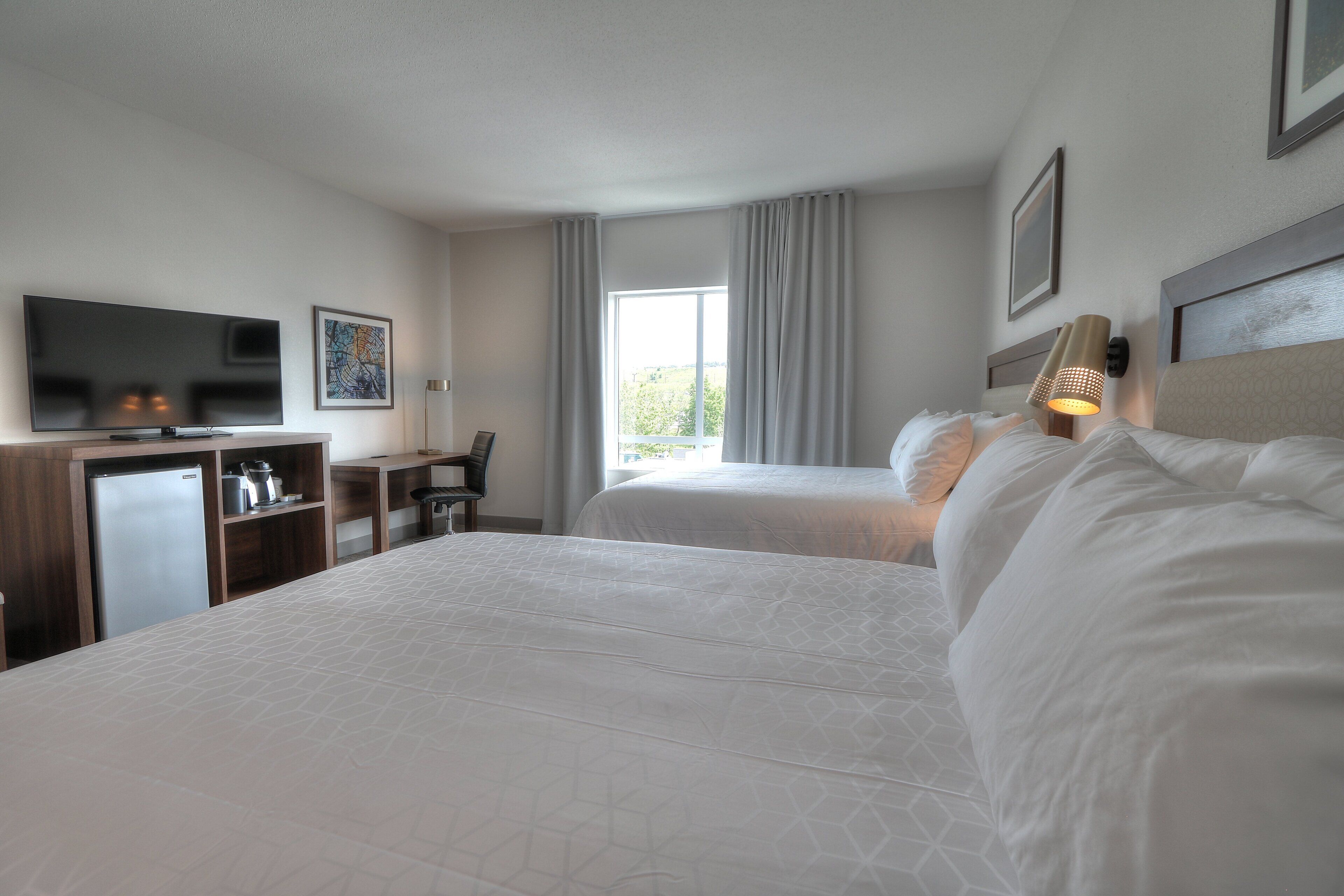 A hotel room with two beds, a TV, a desk, and a window with curtains.