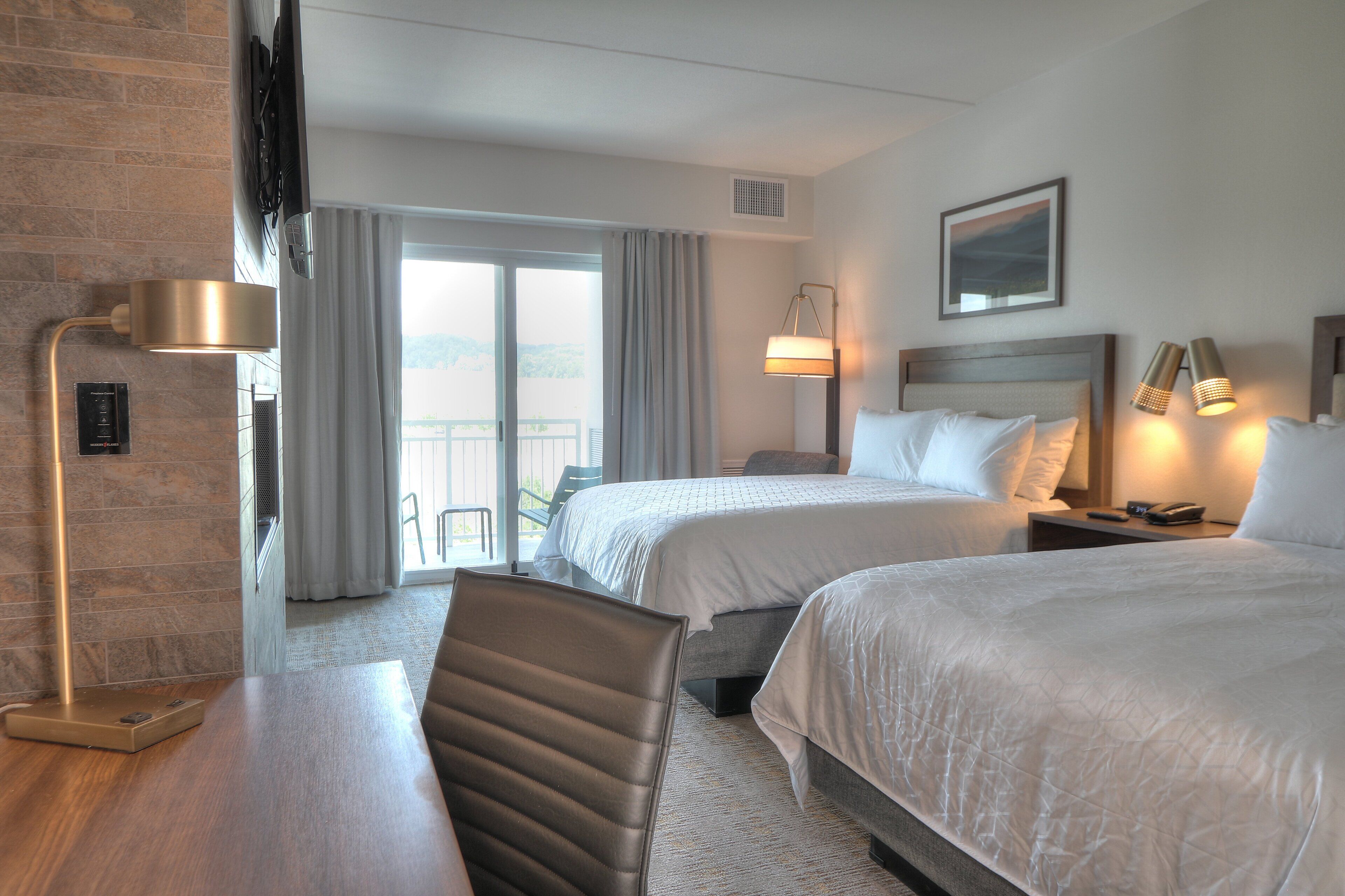 A hotel room with two beds, a desk, a chair, a TV, a window with curtains, and a view of the outdoors.