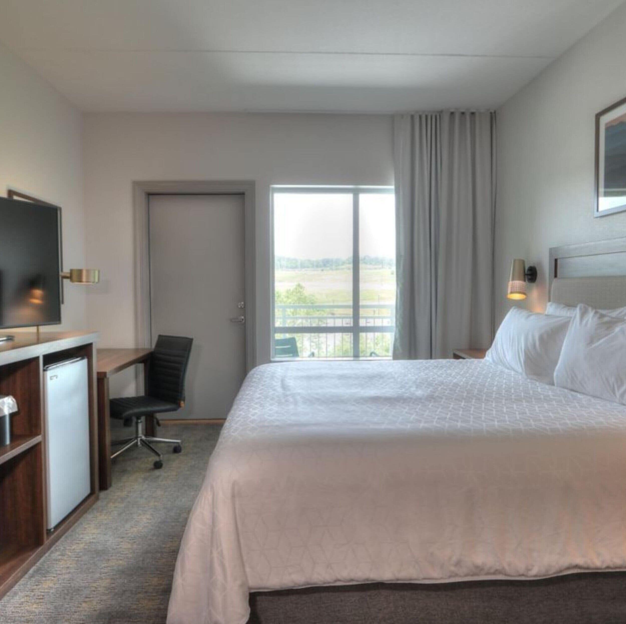 A hotel room with a bed, a desk, a chair, a television, and a window with curtains.