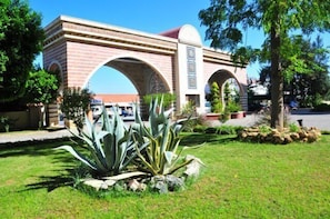 A brick building with arched entrances and a landscaped garden with agave plants. - Nova Park (Manavgat)