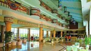 Un vestíbulo amplio con varias zonas de estar, ventanas grandes y columnas decorativas.
