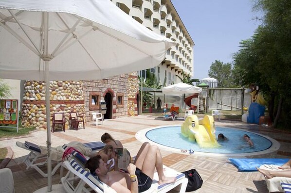 A pool area with lounge chairs, a water slide, and a stone wall. - Nova Park (Manavgat)