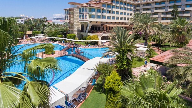 Un hotel con una piscina grande, palmeras y un cielo azul despejado.